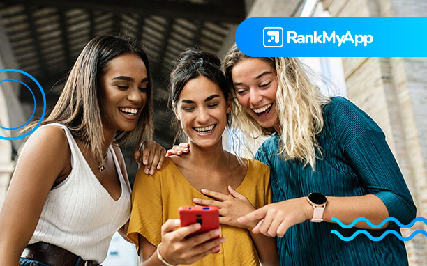 Três mulheres sorrindo e observando um celular.