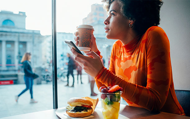Mulher bebendo café e mexendo no celular, remete a aplicações do 5g nas práticas do dia a dia.