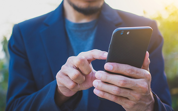 homem branco de terno azul teclando em um celular com capa preta